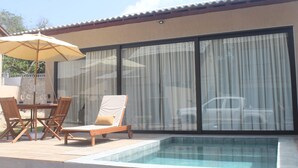 Un área de piscina con mesa y sillas, un sillón de descanso y una sombrilla grande.
