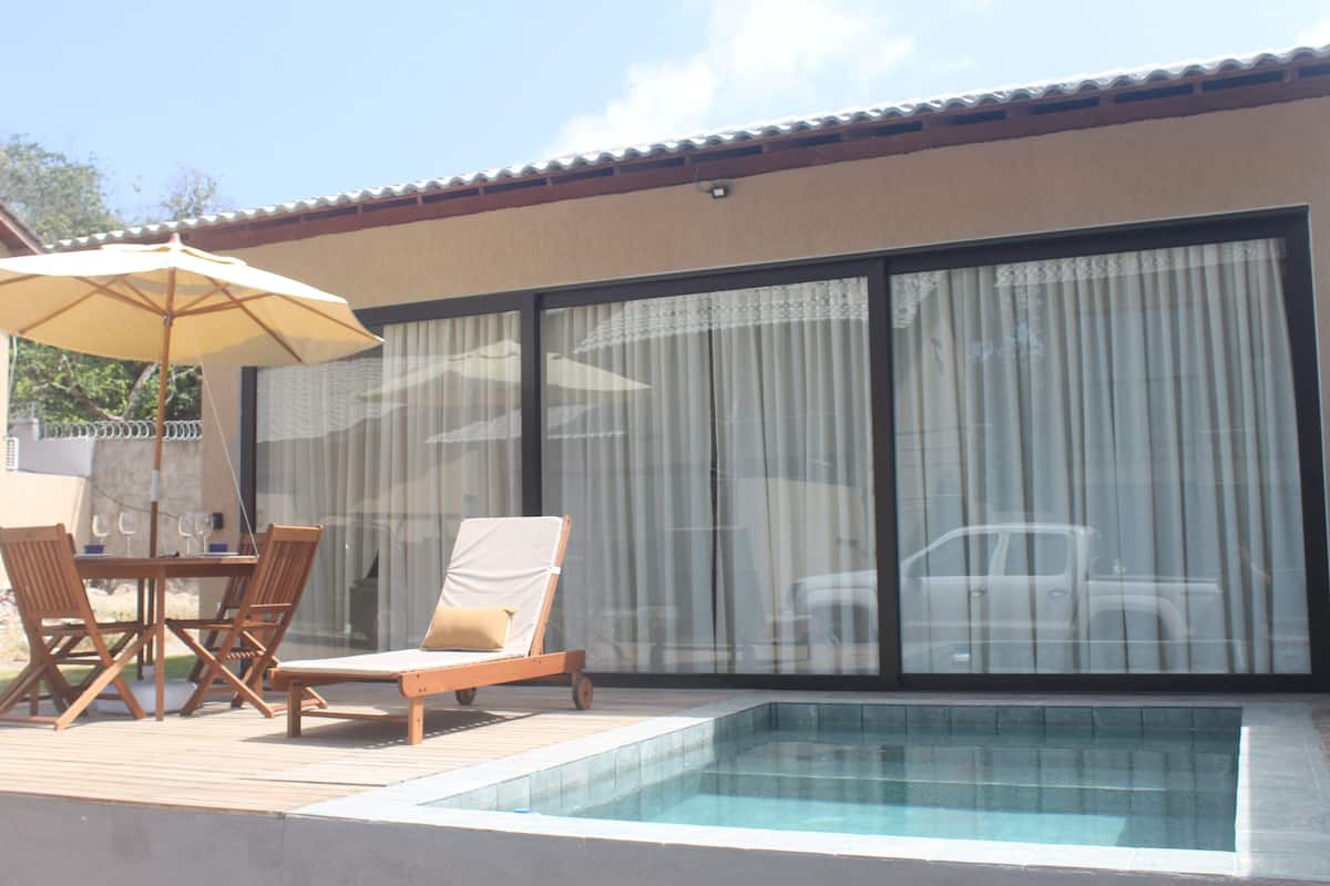 A pool area with a table and chairs, a lounge chair, and a large umbrella.