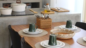 Una mesa de comedor dispuesta con platos, tazones y tazas verdes, junto con utensilios de cocina en una cesta.