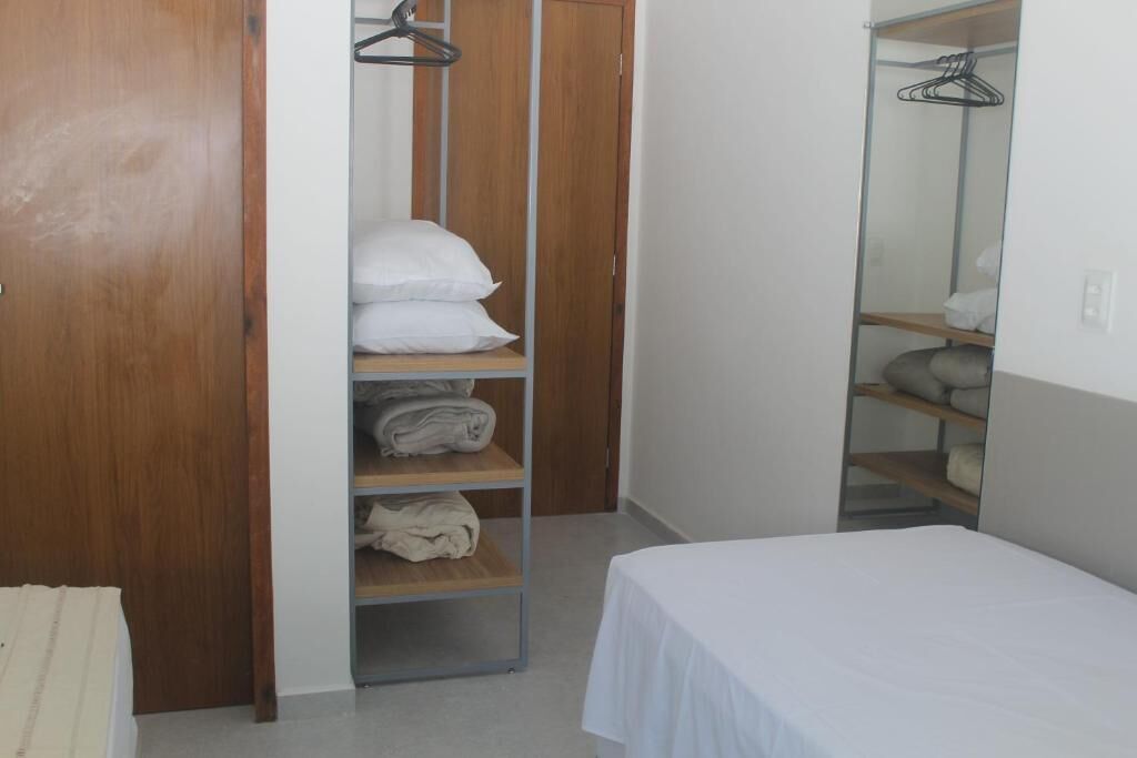 A bedroom with a bed, a wooden wardrobe, and a shelf with folded clothes.