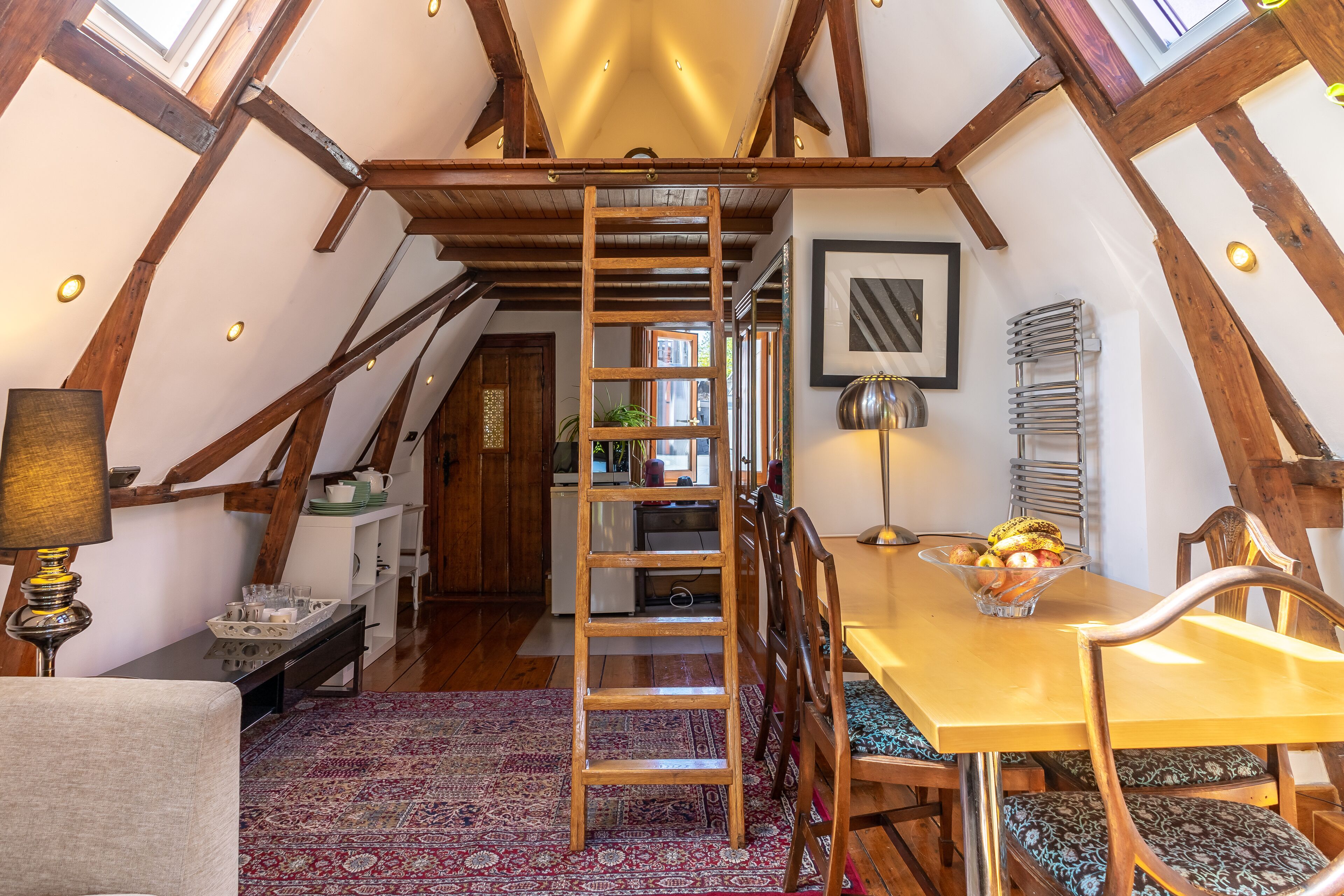 A cozy dining area with a wooden table, chairs, and a ladder leading to an upper level.