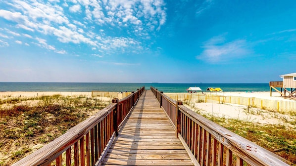 Una passerella di legno conduce a una spiaggia con spiaggia sabbiosa e cielo azzurro limpido.