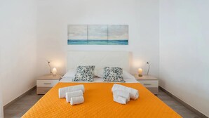 A hotel room with a bed, two nightstands, a painting of a beach, and towels on the bed. - Cozy sea view rooms with private beach and jacuzzi (Lido di Noto)