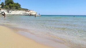 A beach with clear shallow waters, a sandy shore, and rocky cliffs in the background. - Cozy sea view rooms with private beach and jacuzzi (Lido di Noto)
