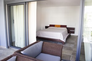 A hotel room with a bed, a wicker sofa, and a sliding glass door leading to a balcony.