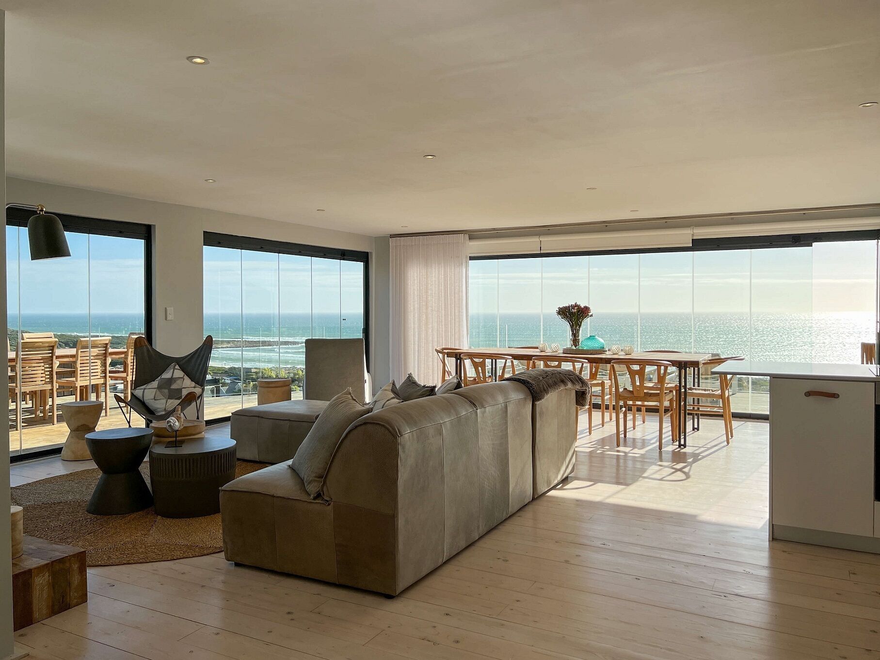 A spacious living area with a large sofa, dining table, and chairs, overlooking a scenic ocean view.