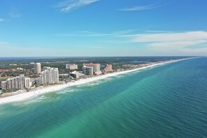 An aerial view of a coastal city with high-rise buildings along the beachfront, clear skies, and a wide expanse of ocean.