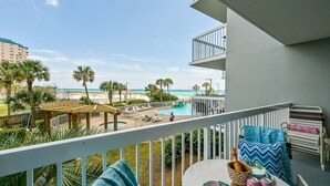 A balcony with a pool, beach view, and outdoor seating area.