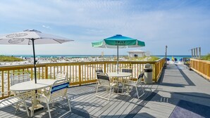 A wooden deck with outdoor seating and umbrellas overlooking a beach.