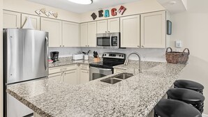 A modern kitchen with a granite countertop, stainless steel appliances, and a 'BEACH' sign on the wall.
