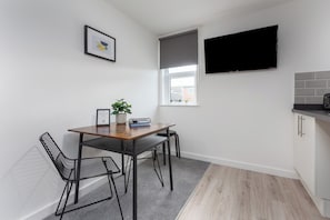 A modern kitchen with a dining area, a flat-screen TV mounted above the window, and a small potted plant on the table.