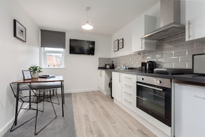 A modern kitchen with a dining area, featuring a built-in oven, a coffee machine, and a large window with a view.
