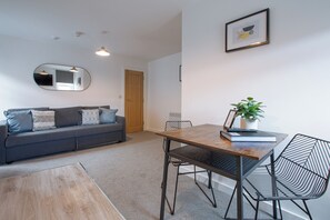 A modern living room with a sofa, a dining table, chairs, a mirror, and a framed picture on the wall.