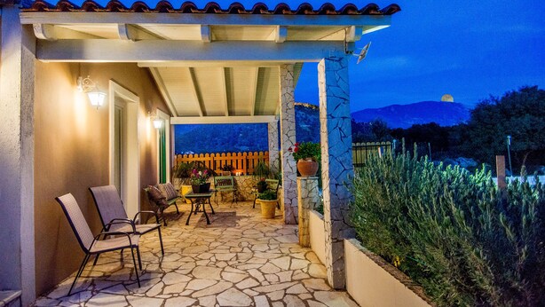 Eine überdachte Terrasse mit Steinböden, Sitzgelegenheiten im Freien und Topfpflanzen.