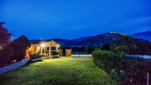 Ein hell erleuchtetes Haus mit Rasen und einem Berg im Hintergrund.