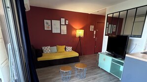 Un salon moderne avec un canapé, deux petites tables, un téléviseur et un miroir.