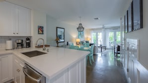 A spacious kitchen with white cabinetry, a large island, and a dining area with teal chairs. - Conch Get Enough at The Truman Annex in Key West (Key West)