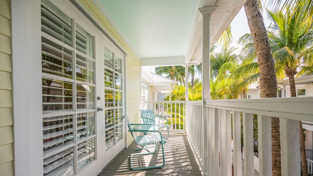A covered porch with a white railing, two rocking chairs, and a view of palm trees. - Conch Get Enough at The Truman Annex in Key West (Key West)