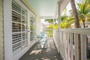 Een overdekt terras met een witte balustrade, twee schommelstoelen en uitzicht op palmbomen.