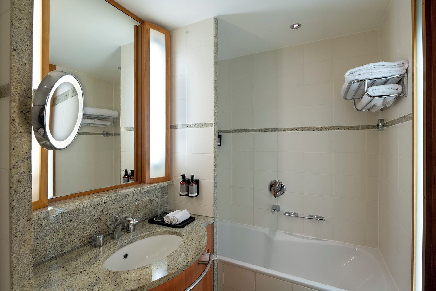 A modern bathroom with a granite countertop sink, a large mirror, a glass-enclosed shower, and a towel rack.