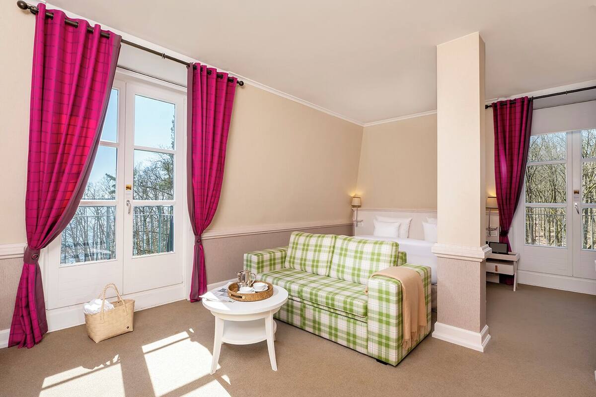 Una habitación con un sofá de tela verde a cuadros, una mesa blanca con una cesta y una ventana con cortinas rosadas.