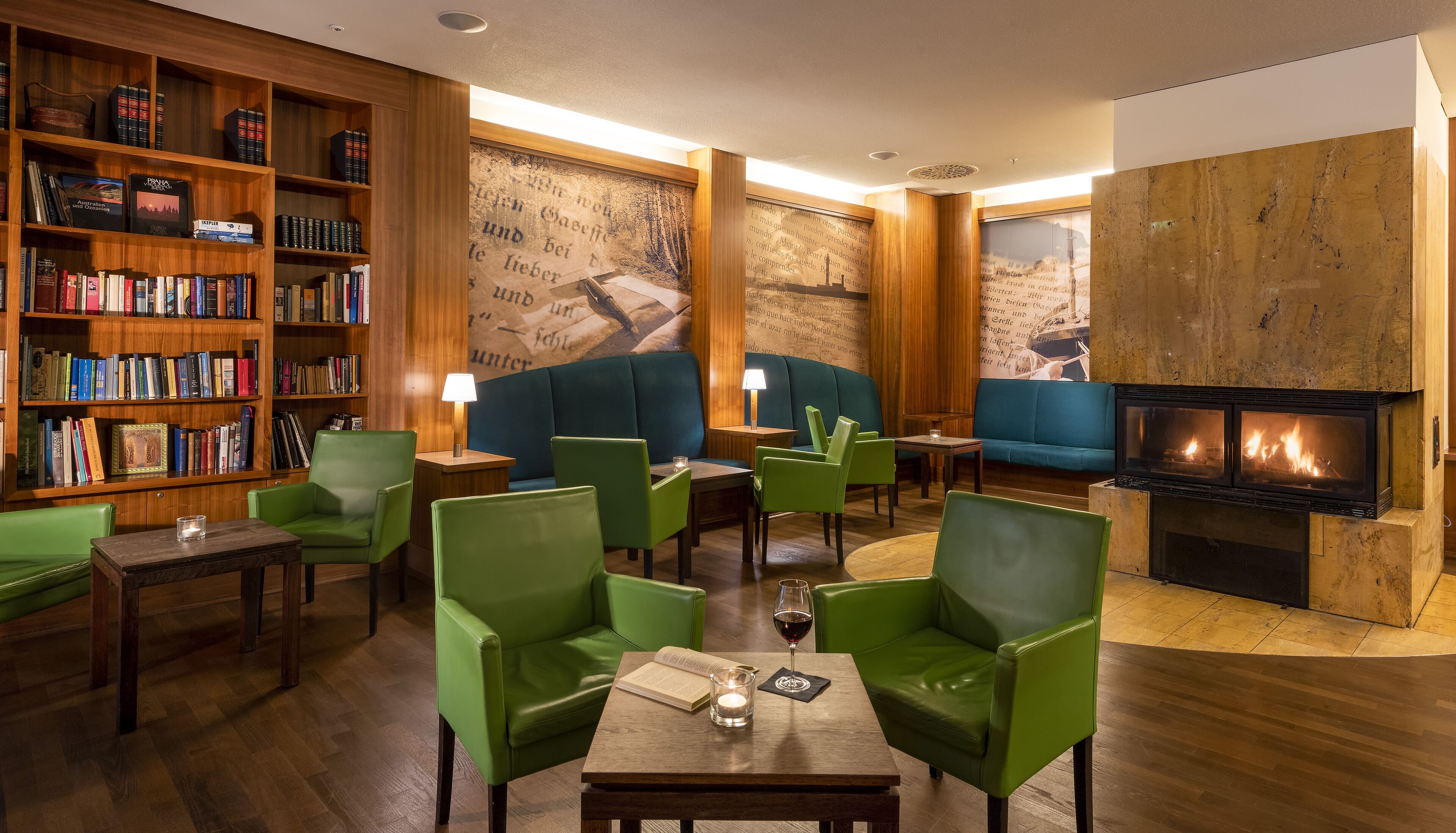 Un rincón tranquilo con sillones verdes, una chimenea y una estantería llena de libros.