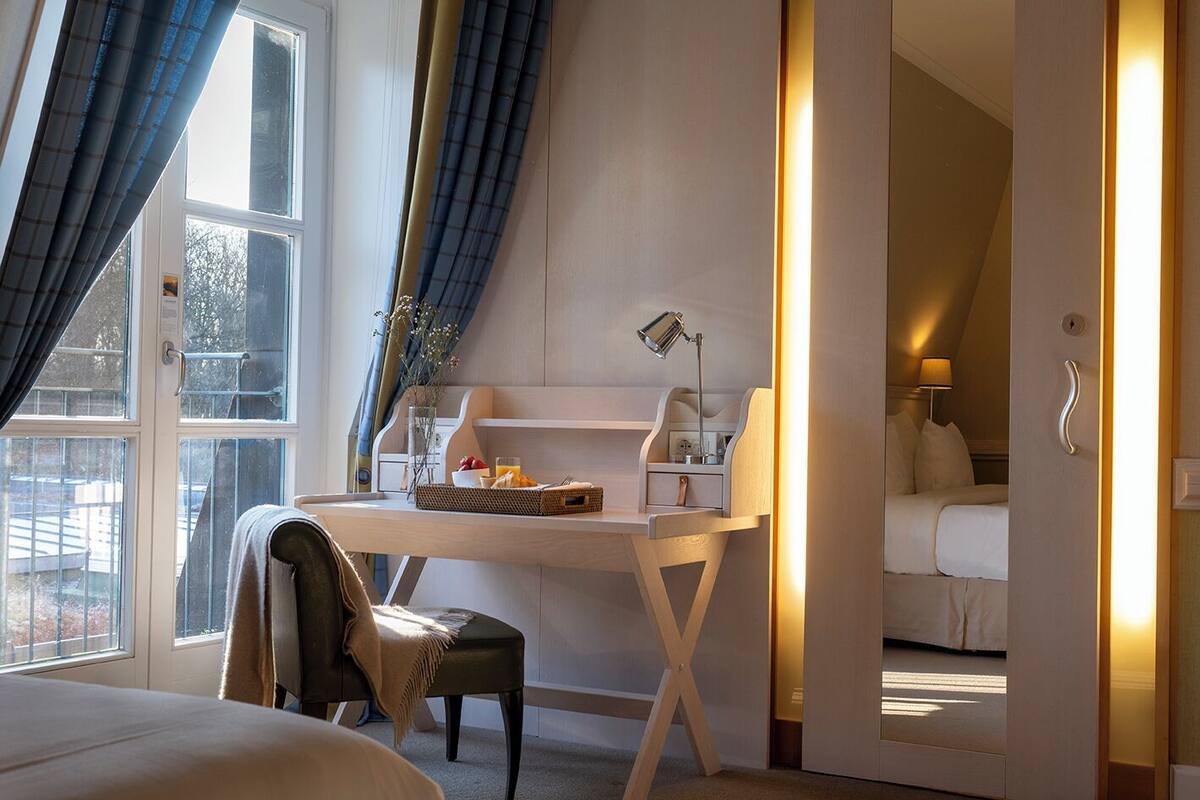 Habitación de hotel con cama, escritorio con lámpara, silla y vista al exterior.