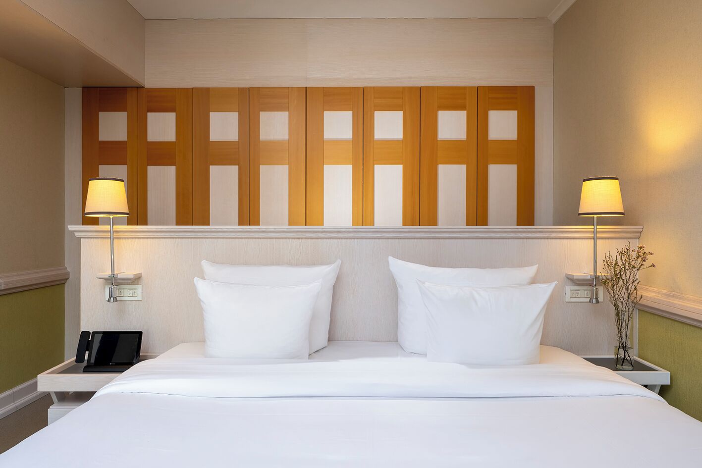 Hotelkamer met een groot bed, twee bedlampen, een televisie aan de muur en een decoratief paneel boven het bed.