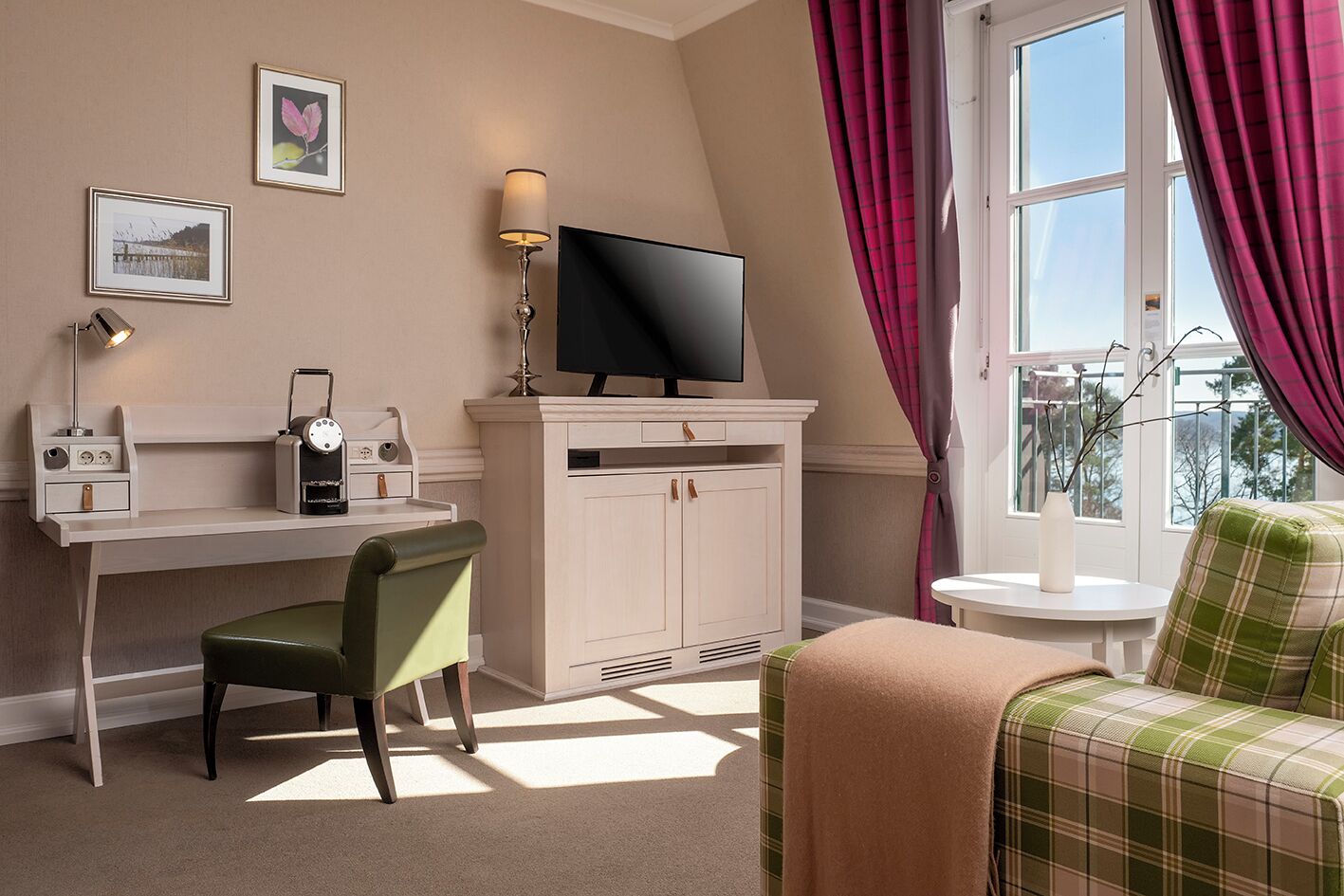 Ein Hotelzimmer mit Schreibtisch, Stuhl, Fernseher und Blick ins Freie.