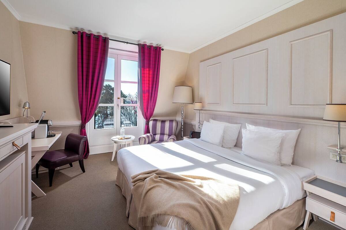 Una habitación de hotel con una cama, un escritorio, una silla, un televisor y una ventana con cortinas.
