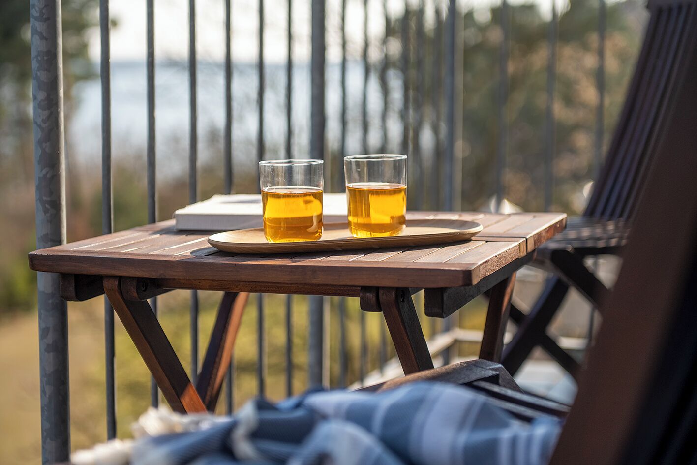 Deux verres contenant un liquide ambré sont posés sur une table en bois, avec une rambarde métallique en arrière-plan.