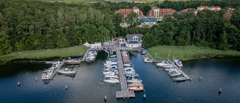A marina with boats docked, surrounded by forested hills and a large building in the background.