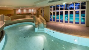 Una amplia piscina cubierta de diseño curvo, una escalera que conduce a un balcón y vistas de la piscina a través de amplias puertas de cristal.