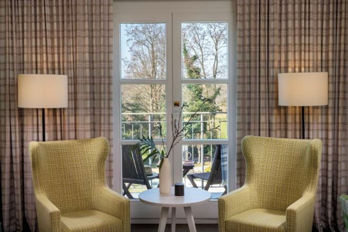 A room with two yellow armchairs, a small round table, and a vase with branches.