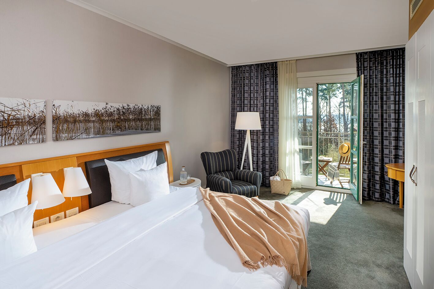 A hotel room with a large bed, a chair, a table, and a view of the outdoors through a glass door.