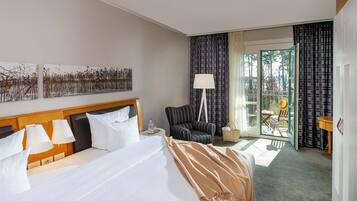 A hotel room with a large bed, a chair, a table, and a view of the outdoors through a glass door.