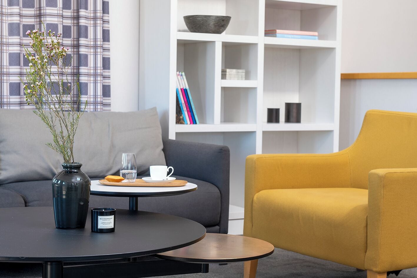 Una sala de estar moderna con una mesa redonda, un sillón amarillo, un sofá gris y una estantería al fondo.