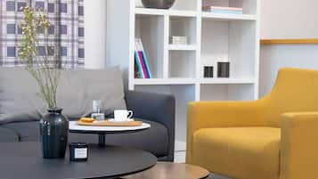 Una sala de estar moderna con una mesa redonda, un sillón amarillo, un sofá gris y una estantería al fondo.