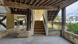 Escada de madeira que dá acesso a um andar superior, sustentada por vigas e colunas de madeira, com piso de concreto e vista para um estacionamento.
