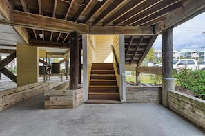 A wooden staircase leading to a covered area with a concrete floor, surrounded by wooden beams and columns.