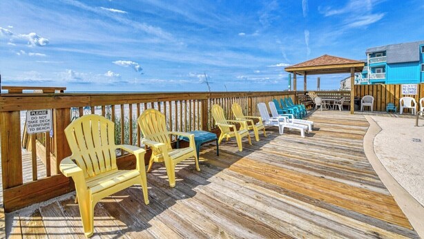 Um deck de madeira com cadeiras Adirondack, uma área coberta e vista para o oceano.