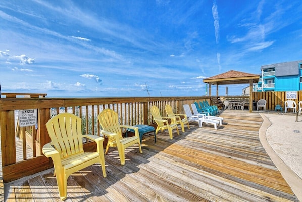 A wooden deck with Adirondack chairs, a covered area, and a view of the ocean.