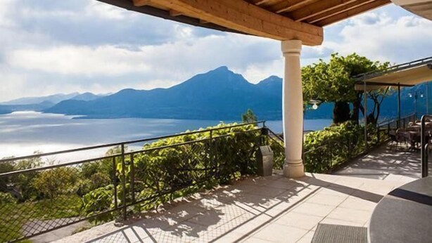 A terrace with a view of mountains and a lake, wooden pergola, and outdoor seating.