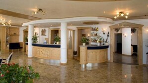 A spacious lobby with a curved reception desk, multiple columns, and a polished marble floor.