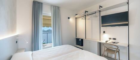 Una habitación de hotel moderna con una cama grande, un escritorio con silla, un televisor de pantalla plana y un balcón con cortinas.