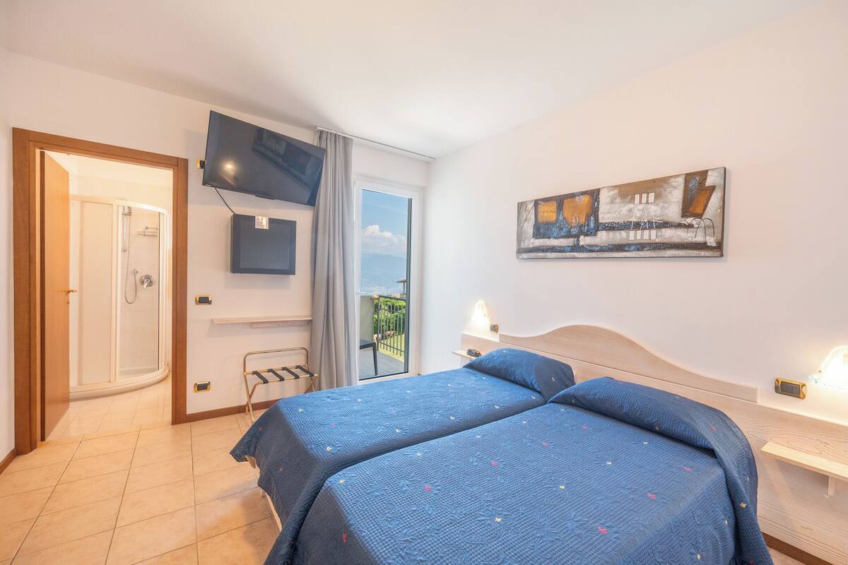 A hotel room with two beds, a TV, a painting, and a balcony with a view.