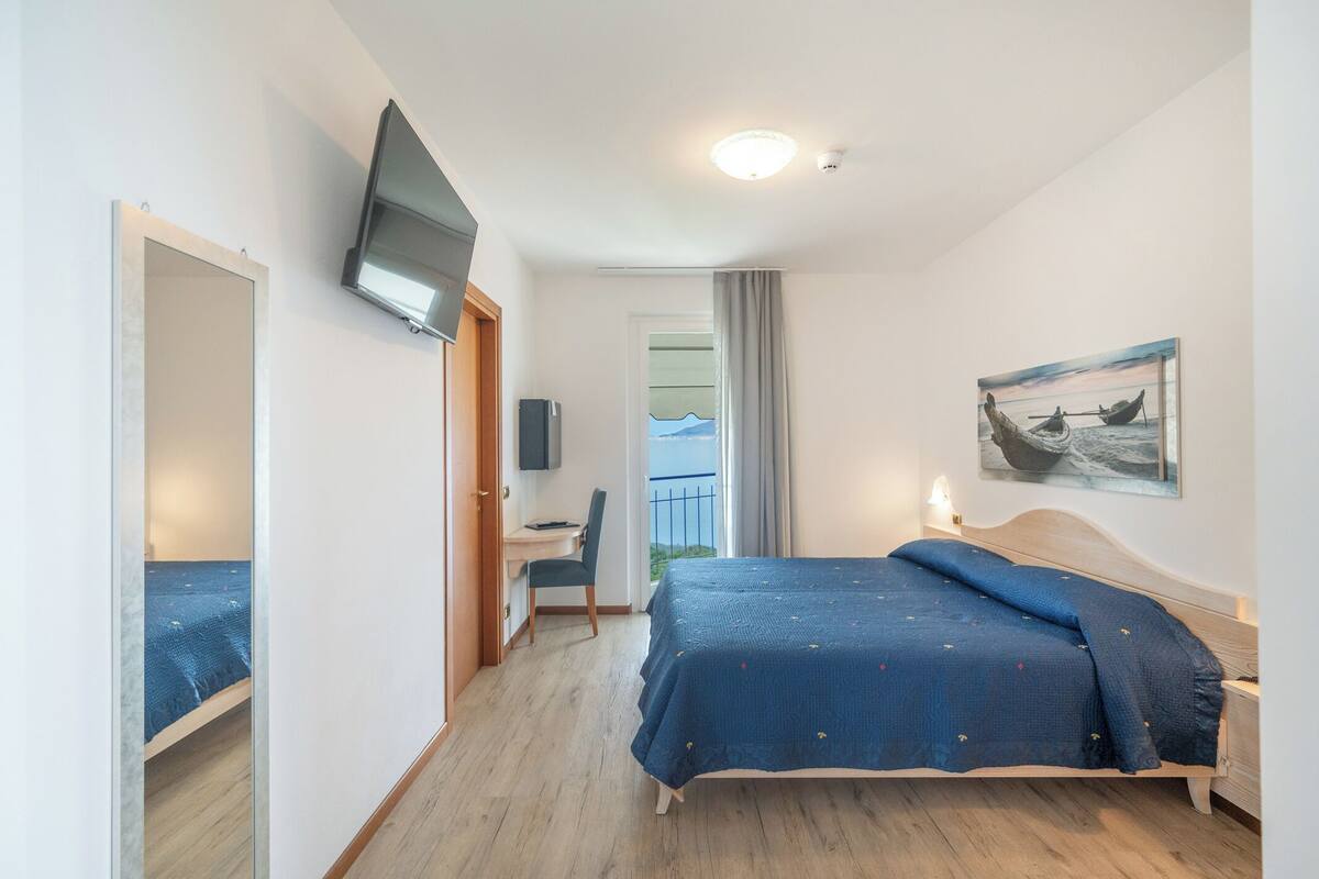 A hotel room with a bed, a desk, a chair, a TV, and a painting.