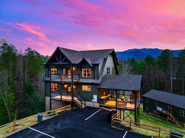 Un grand chalet à plusieurs étages, doté d’un balcon et d’un espace extérieur aménagé, entouré de forêt et de montagnes.