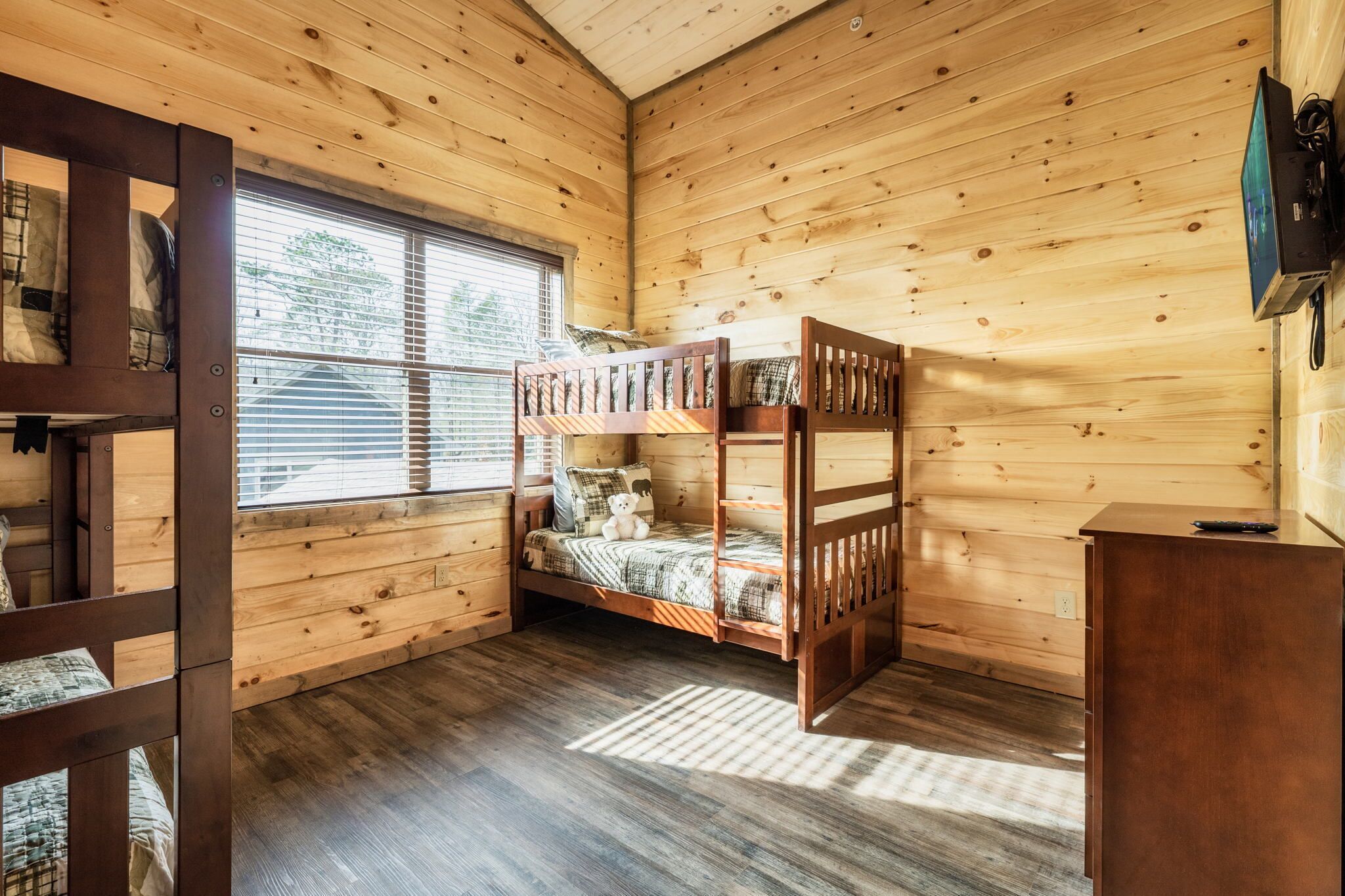 Habitació de cabana de fusta amb lliteres, una finestra i televisió penjada a la paret.