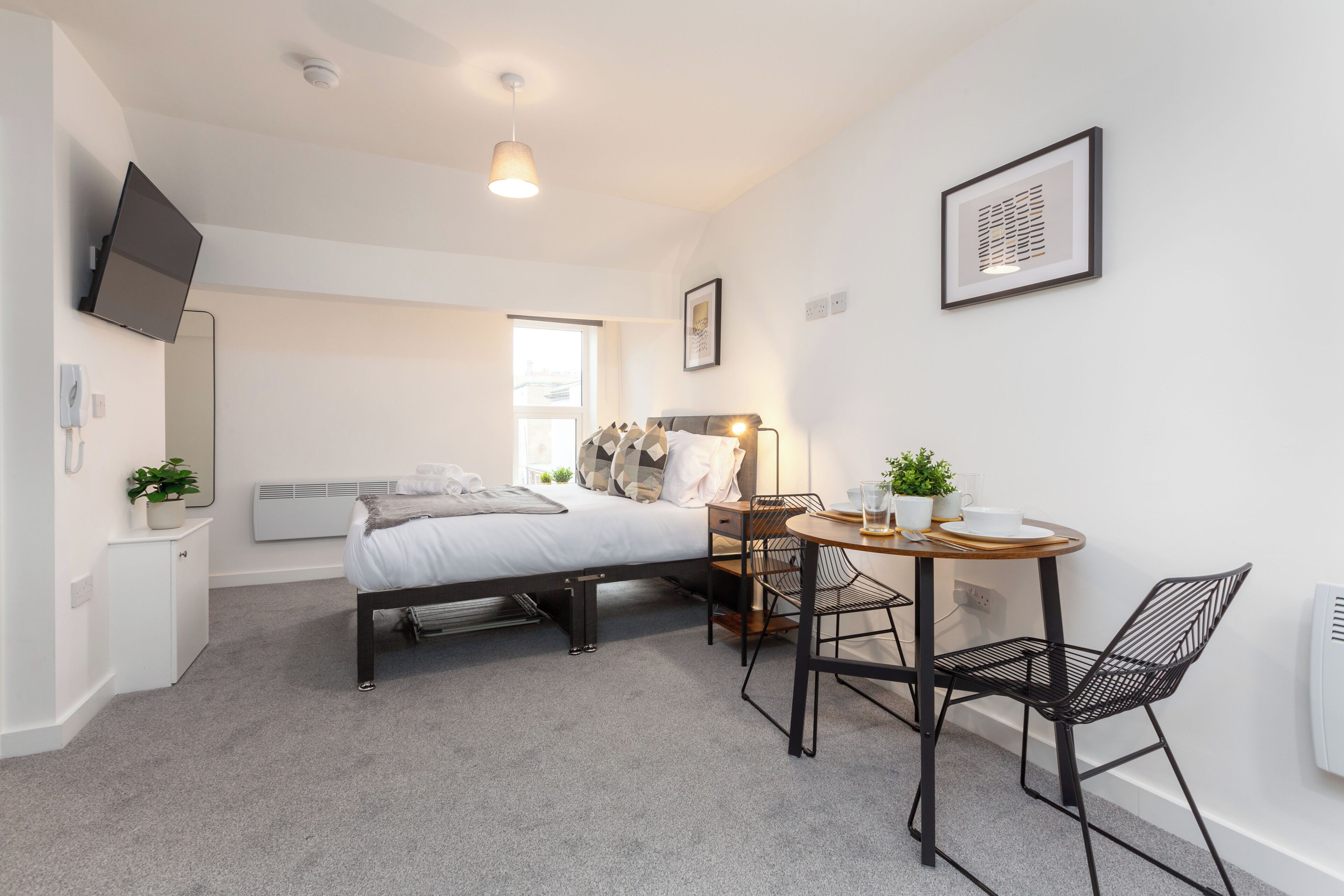 A modern bedroom with a bed, bedside table, and a small dining area with chairs and a table.